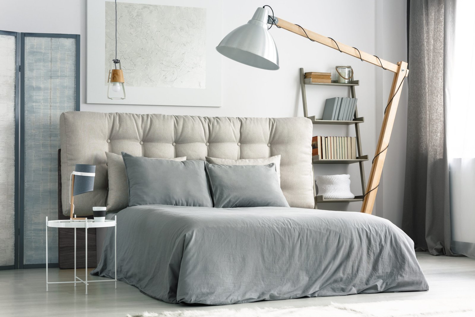 Big wooden lamp near comfortable bed with grey bedding