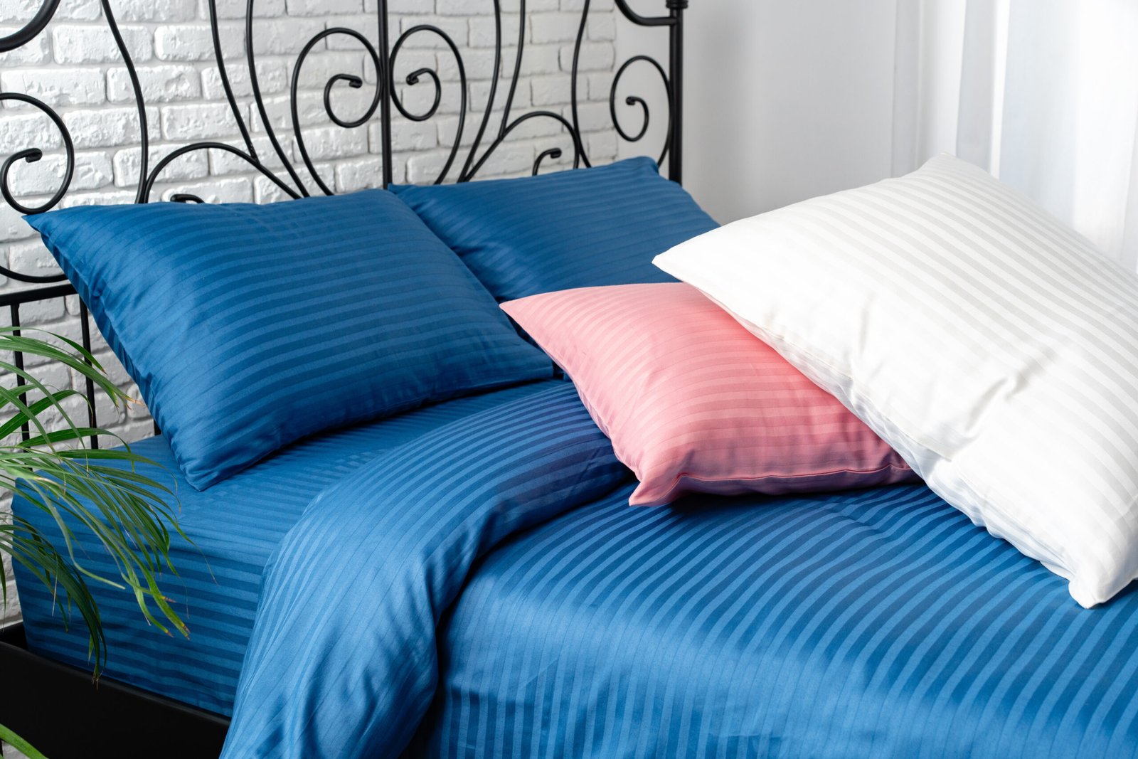 A close-up view of a bed with blue striped bedding and a black iron headboard.