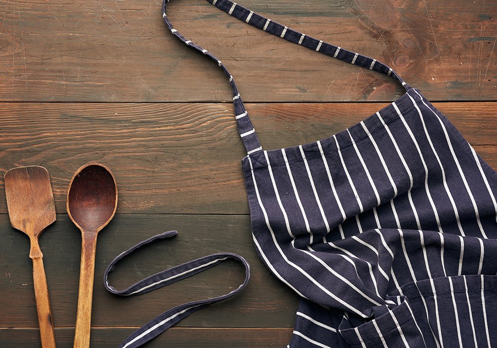 blue textile kitchen apron with white stripes and wooden spoons, top view