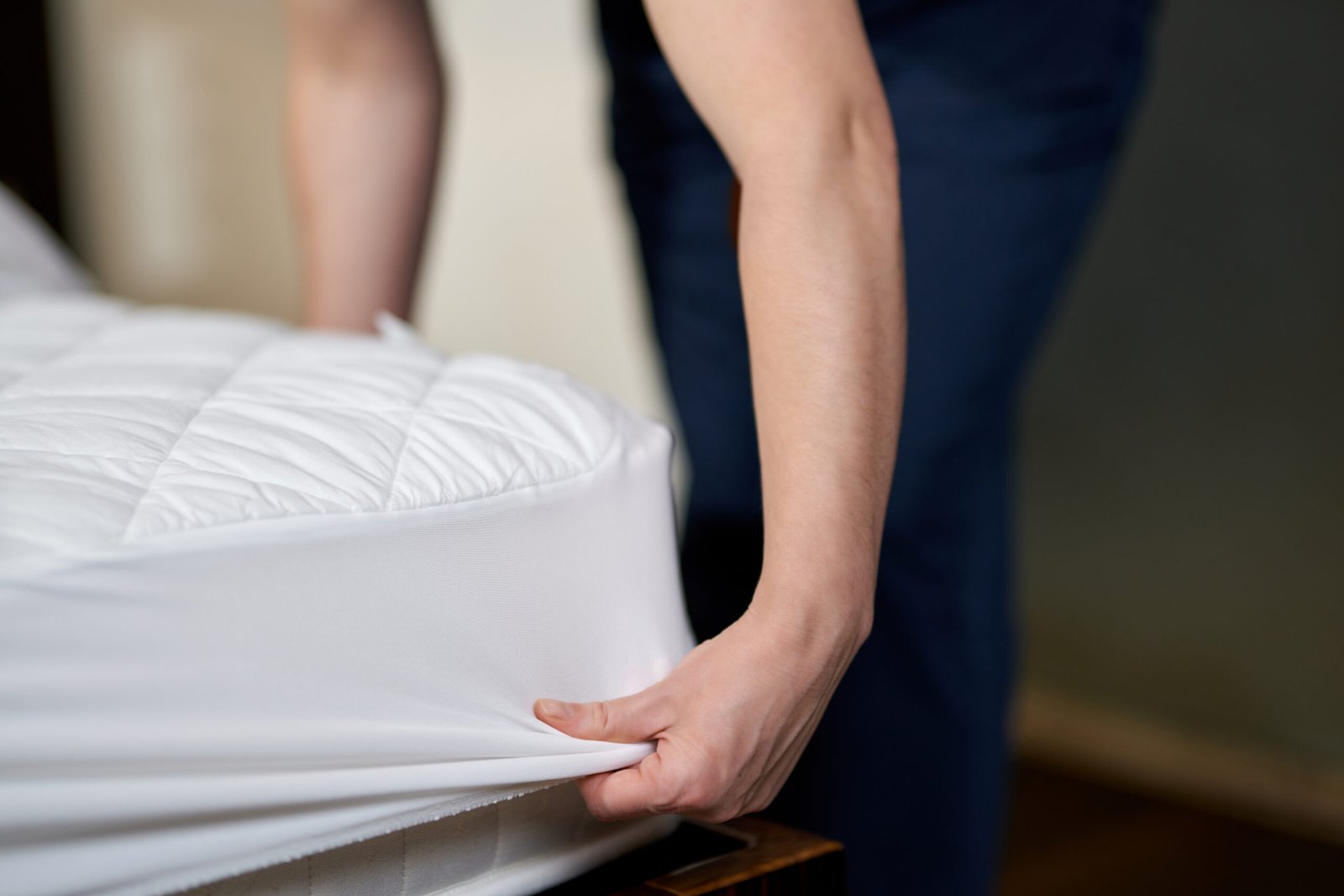 Cropped phot of woman changing clean sheet on white mattress while cleaning in hotel room. Hotel service concept