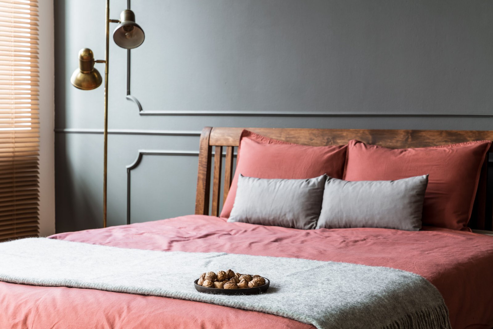 Close-up of grey blanket on pink bed in hotel bedroom interior with gold lamp