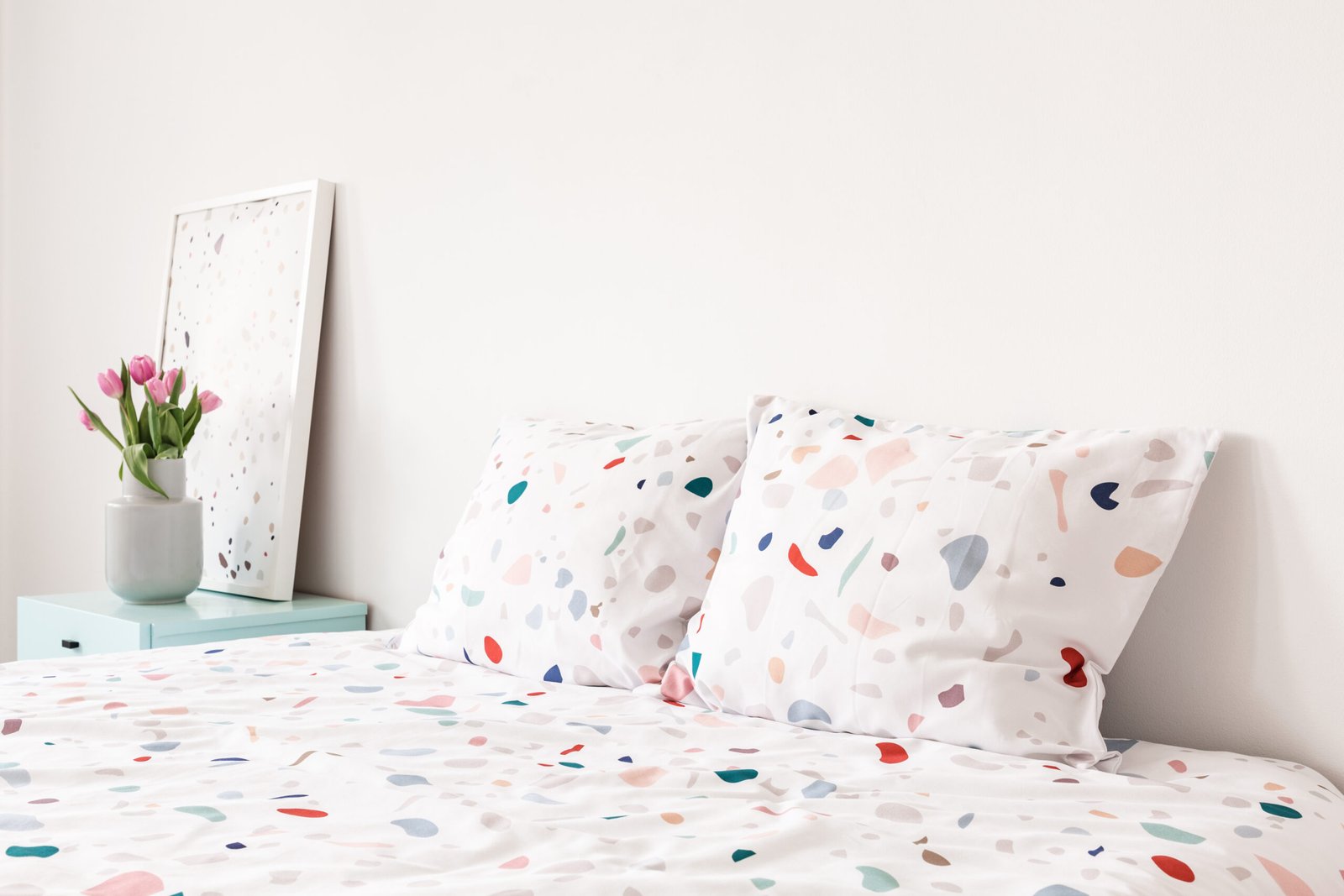 Close-up of dotted pillows and sheets next to bedside table with vase of tulips in a bright bedroom interior