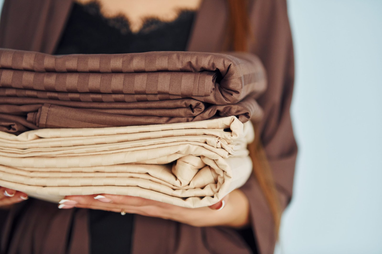 Close up view of young woman that standing against wall with bed clothes in hands.