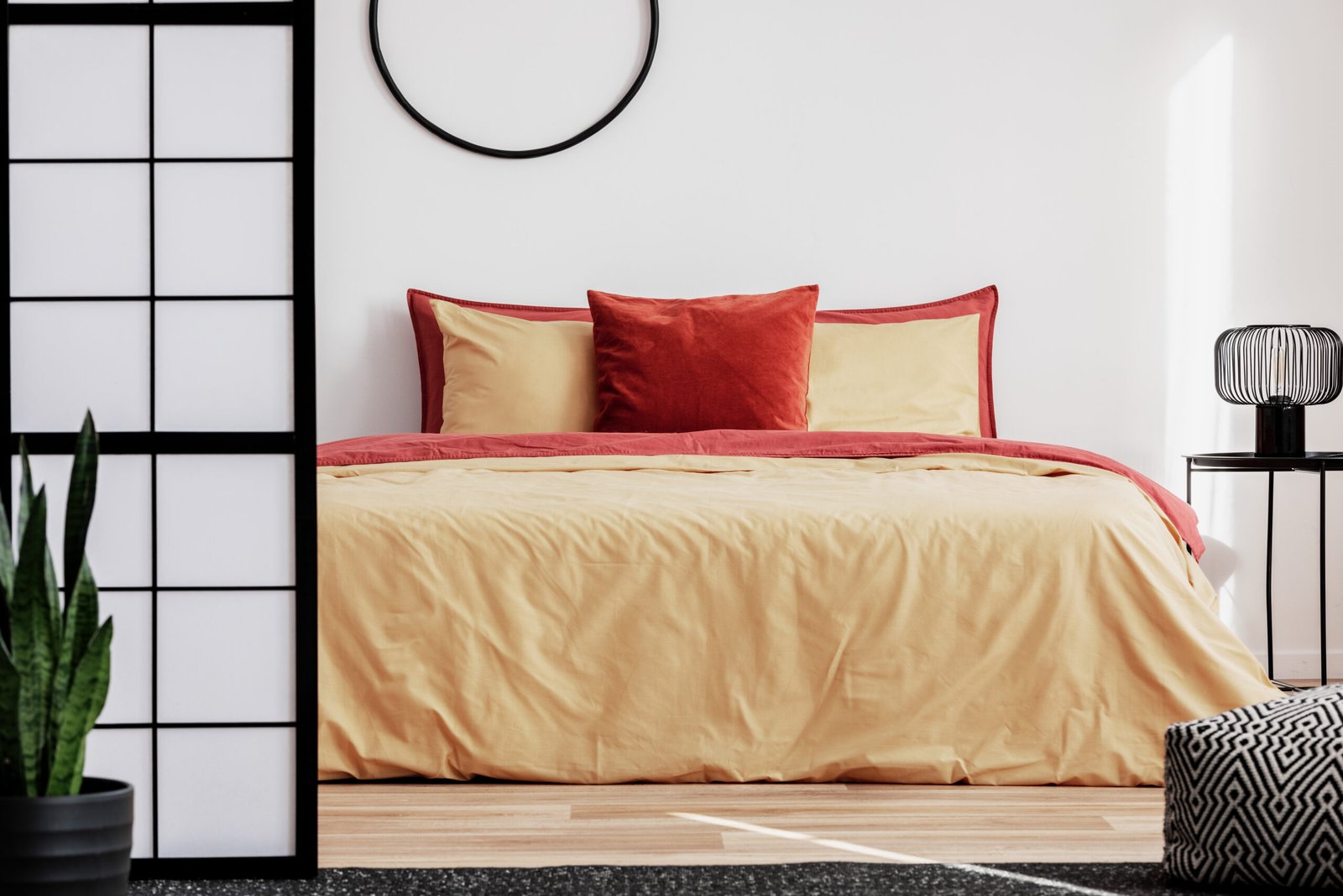 Comfortable bed with yellow and red bedding, industrial lamp on bedside table