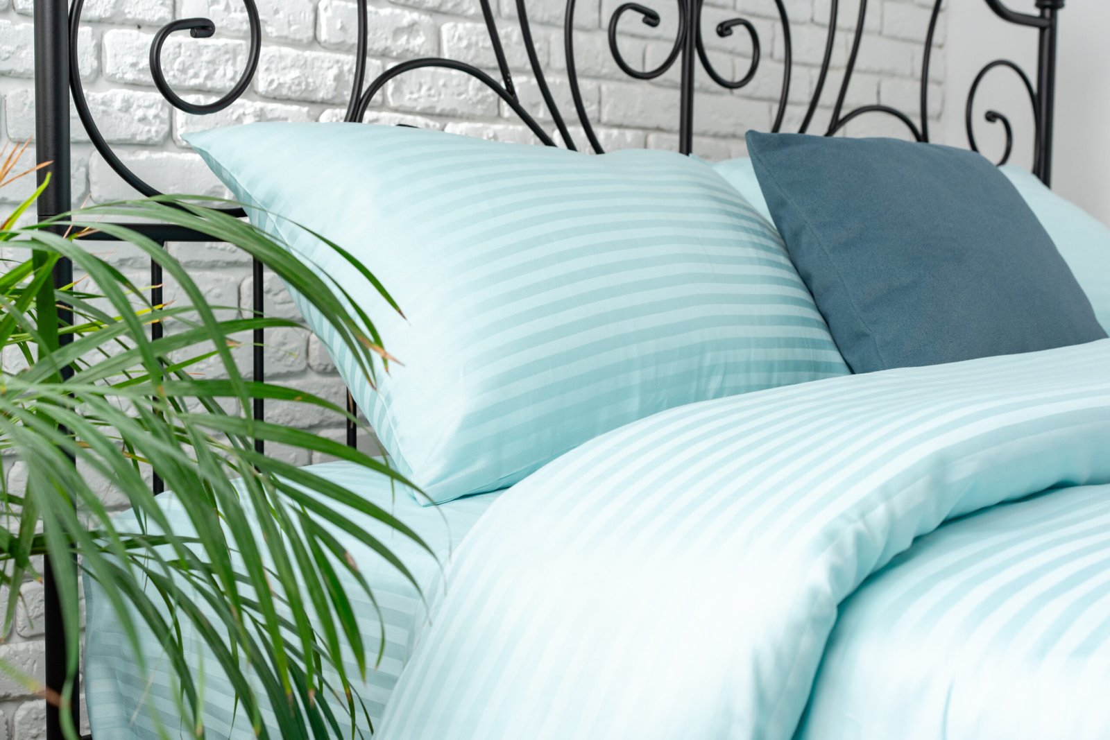 A close-up shot of a mint green, striped bedspread with a matching pillow on a black metal framed bed.