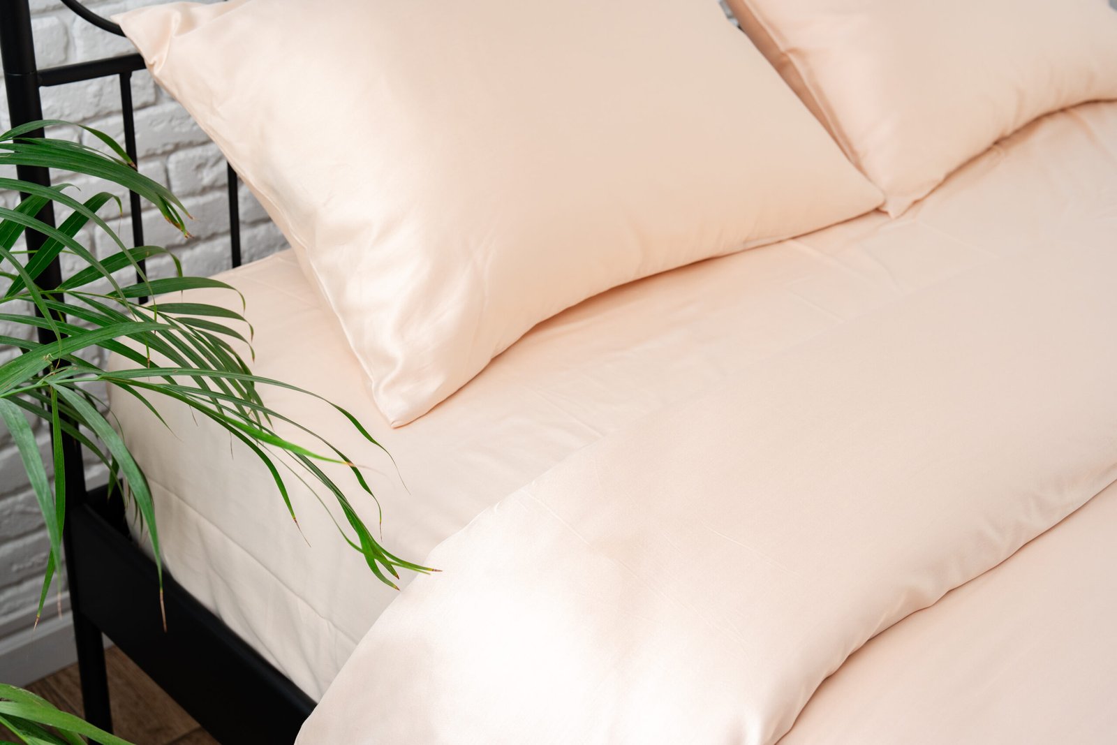 A close up of two peach pillowcases resting atop a black wrought iron bed frame, set against a white brick wall backdrop.