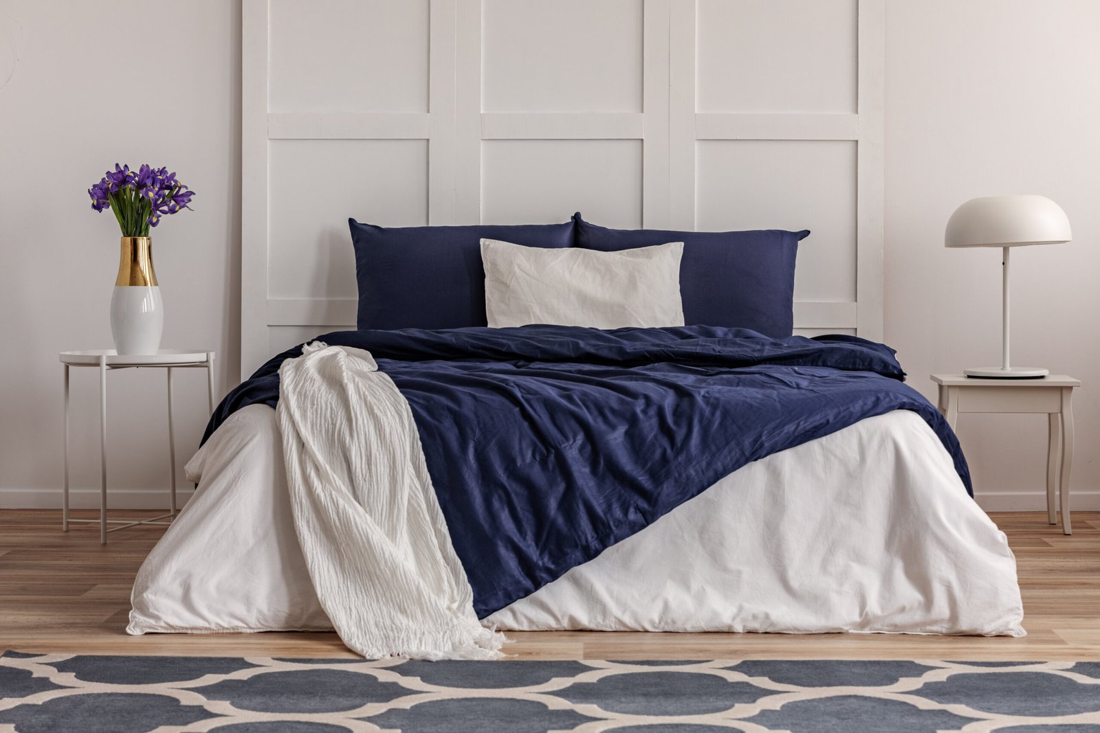 Purple flowers in white vase on elegant nightstand in fashionable bedroom interior