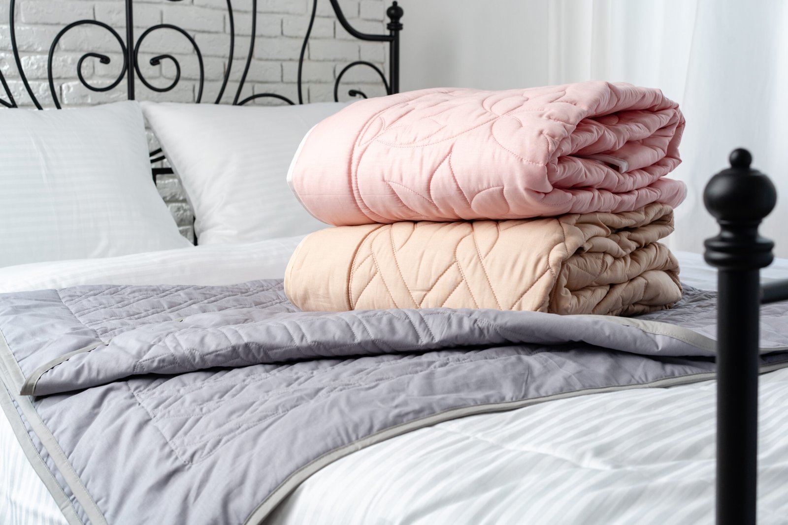 Two quilted blankets in pink and peach are neatly stacked on top of a gray bedspread.