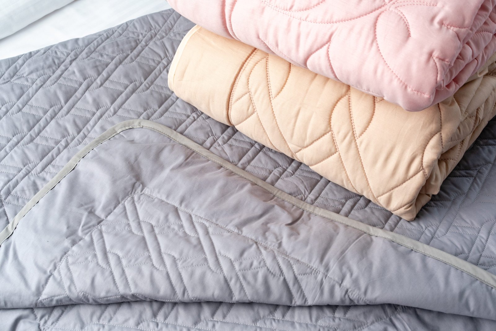Two quilted blankets in pink and peach are neatly stacked on top of a gray bedspread.